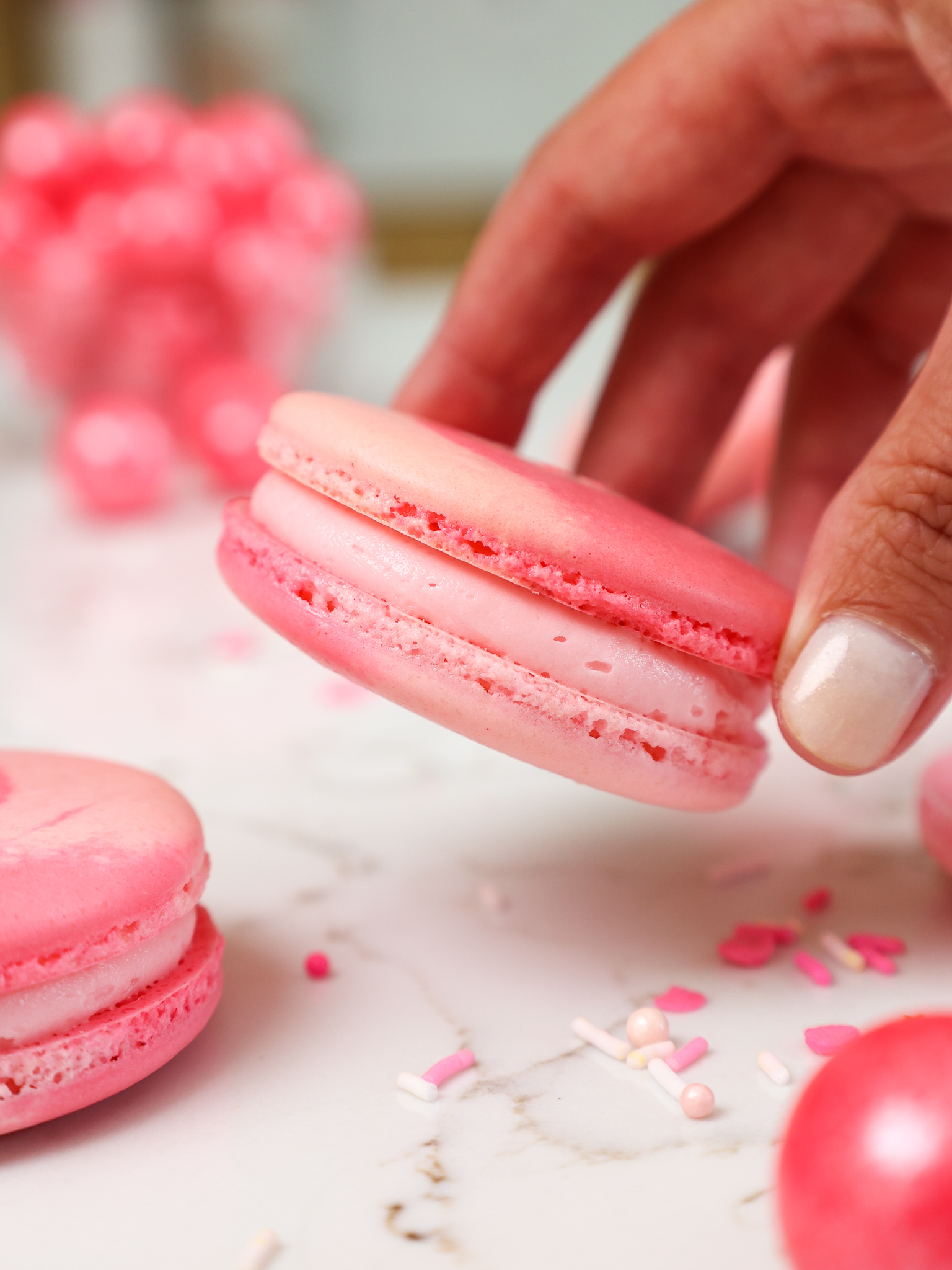image of a bubblegum macaron being held up to show it's bubblegum frosting filling