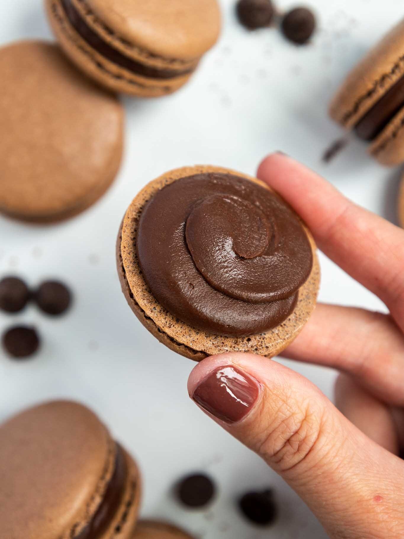 image of a dark chocolate macaron shell being filled with dark chocolate ganache