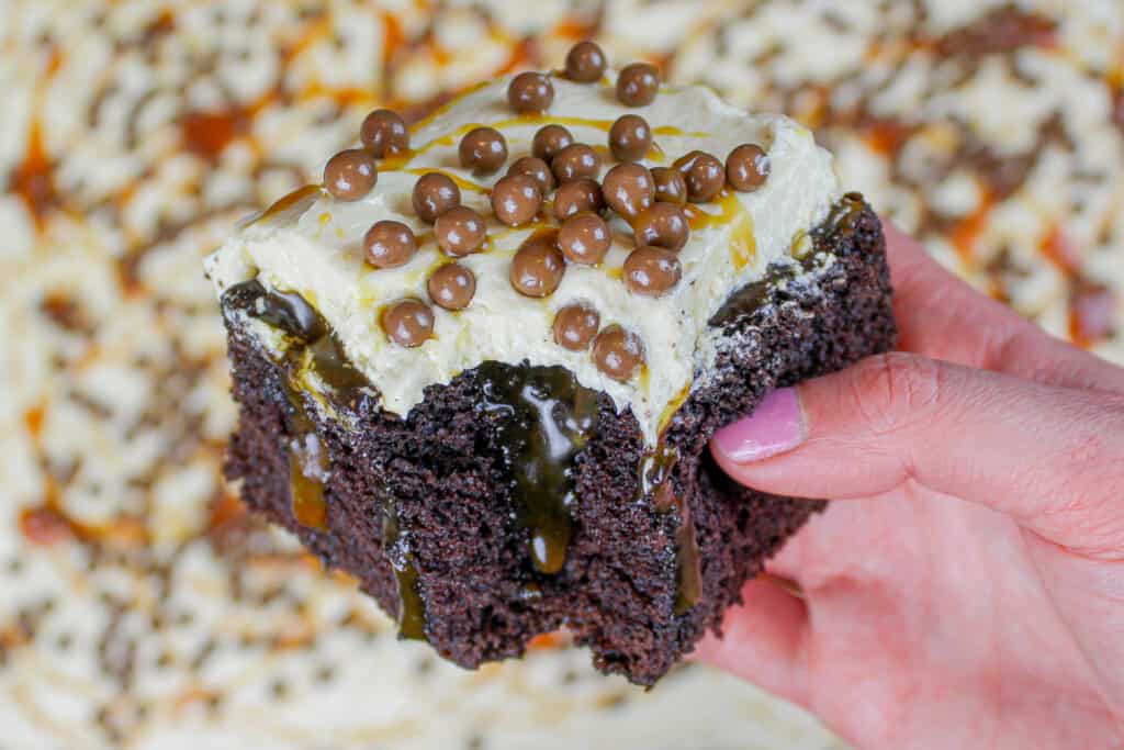 image of chocolate caramel poke cake slice held in hand to show homemade caramel sauce oozing out
