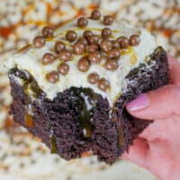 image of chocolate caramel poke cake slice held in hand to show homemade caramel sauce oozing out