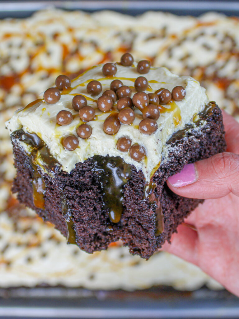 image of a chocolate caramel poke cake slice being held up to show it's caramel filling