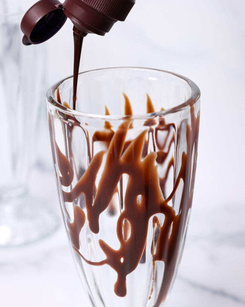 image of a hurricane glass being lined with chocolate syrup