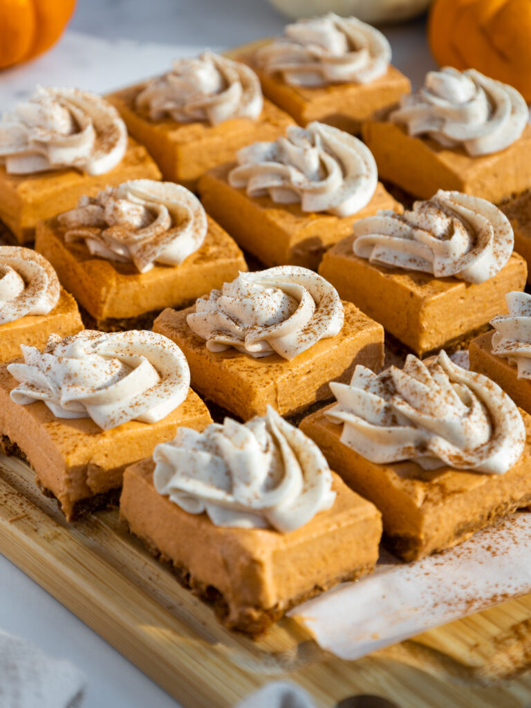 image of no bake pumpkin cheesecake bars that have been cut into squares and topped with whipped cream