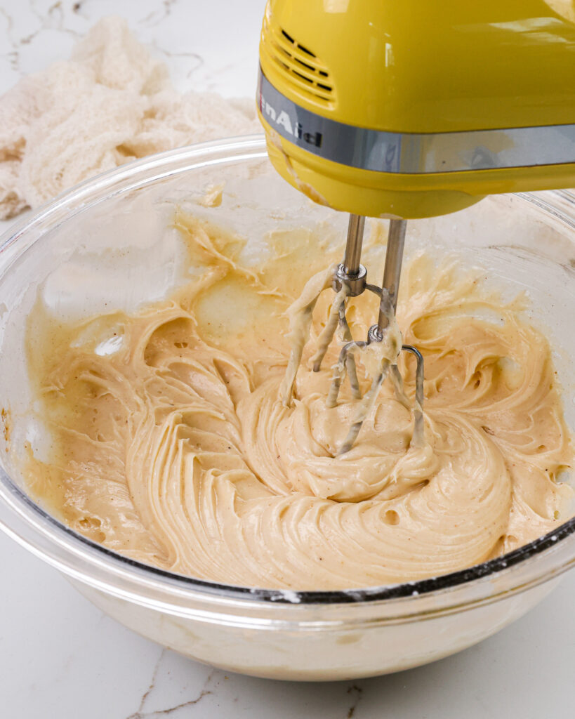 image of spiced cream. cheese frosting that's being made in a bowl with a hand mixer