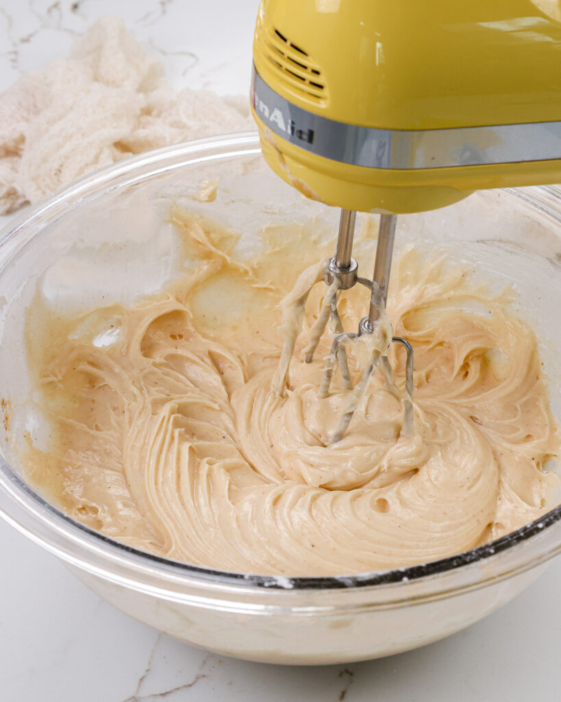 image of spiced cream. cheese frosting that's being made in a bowl with a hand mixer