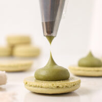 image of matcha ganache being piped on to a matcha macaron shells