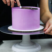 image of a purple cake being frosted with buttercream to have super smooth sides and sharp edges