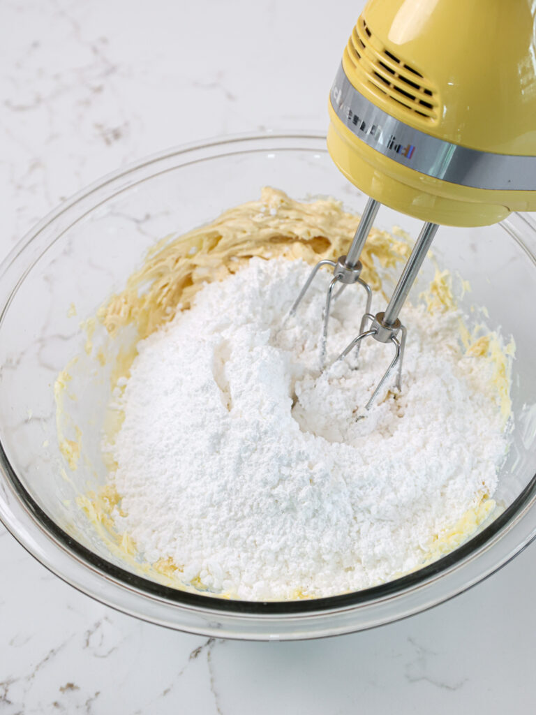 image of powdered sugar being mixed into butter and cream cheese to make homemade cream cheese frosting