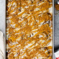 image of biscoff cinnamon rolls baked in a pan and topped with melted cookie butter and crushed biscoff cookies