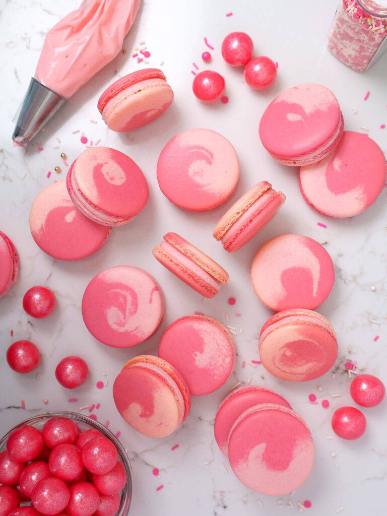 image of bubblegum macarons laid out on a counter to show their two toned pink shells and bubblegum frosting filling