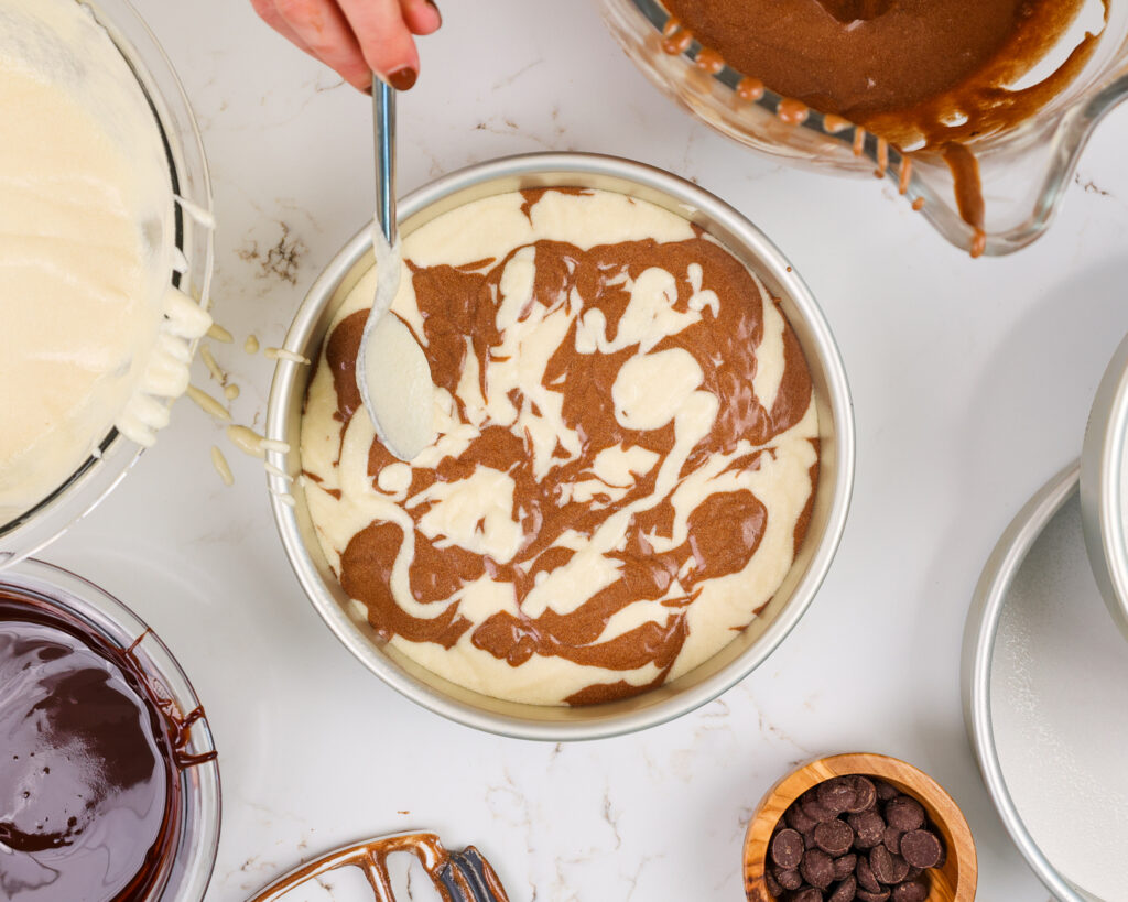 image of vanilla and chocolate cake batter being spooned into an 8-inch cake pan to make a marble layer cake