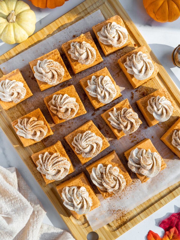 image of no bake pumpkin cheesecake bars that have been cut into squares and topped with whipped cream