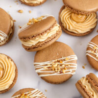 image of peanut butter macarons filled with honey roasted peanut butter buttercream and topped with chopped peanuts and a white chocolate drizzle