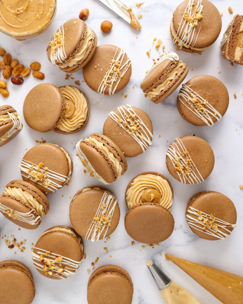 image of peanut butter macarons filled with honey roasted peanut butter buttercream and topped with chopped peanuts and a white chocolate drizzle