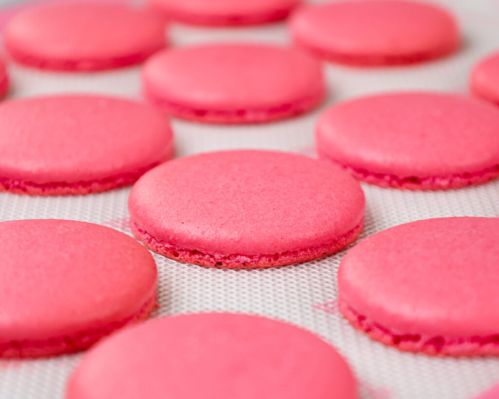 image of pink swiss macaron shells that have been baked and are cooling on a silpat mat