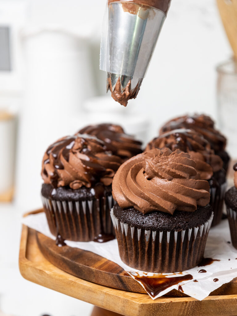 image of chocolate whipped cream frosting that's being piped onto chocolate cupcakes 