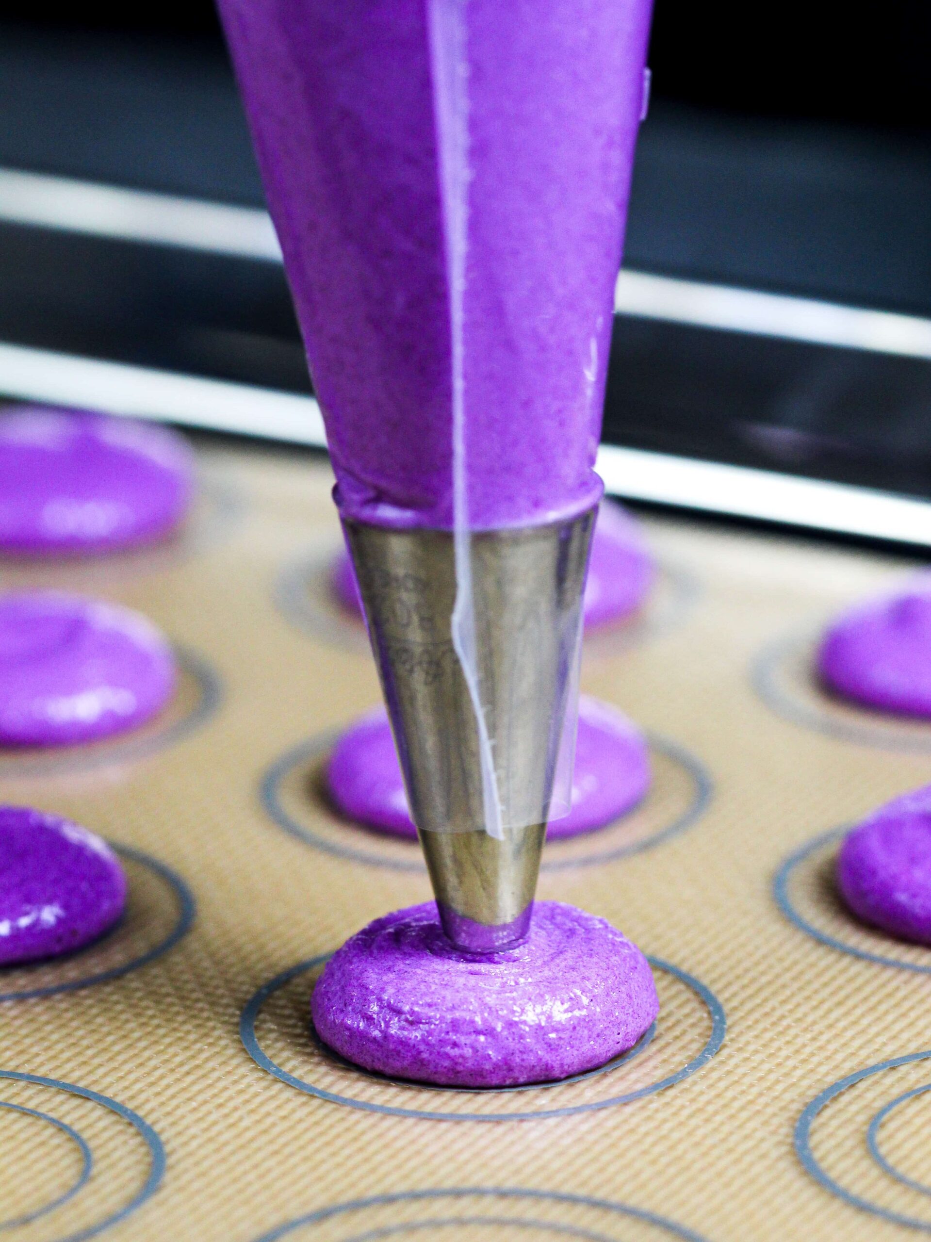 image of purple macarons being piped onto a silpat mat