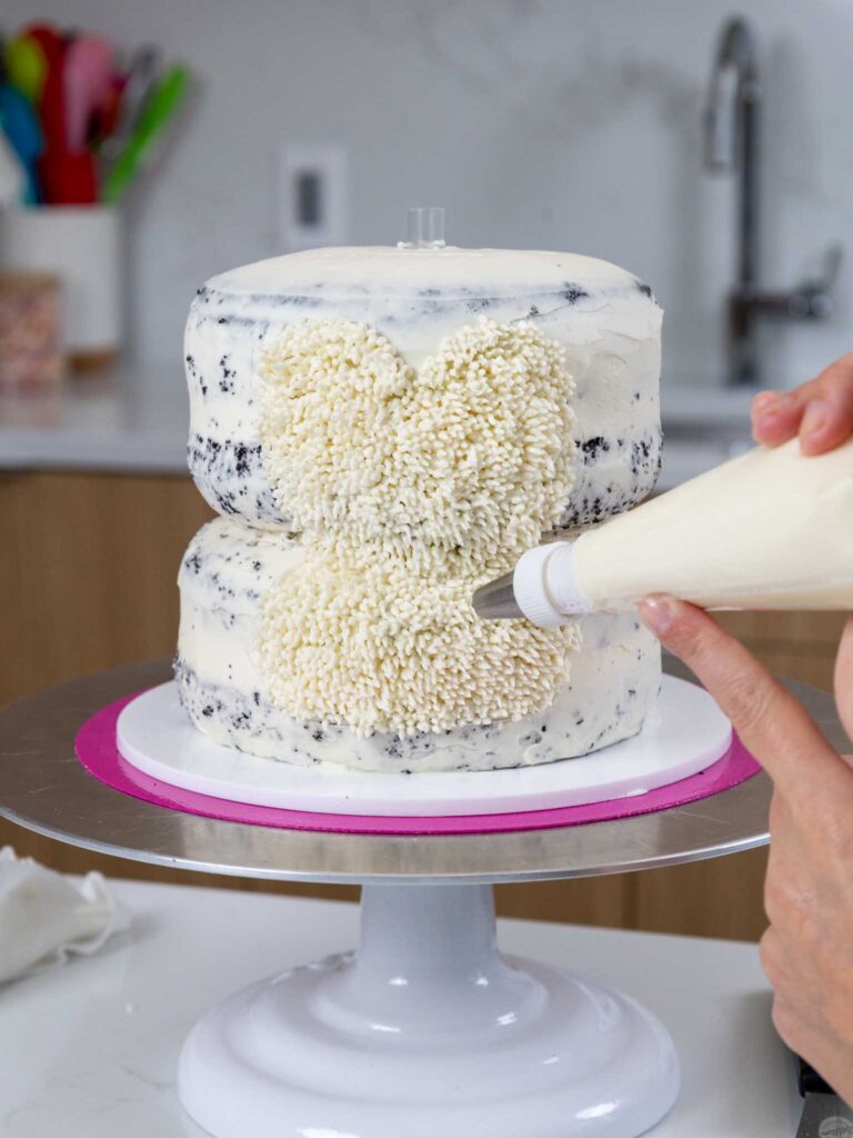 image of white buttercream being piped onto a penguin cake using a small grass piping tip
