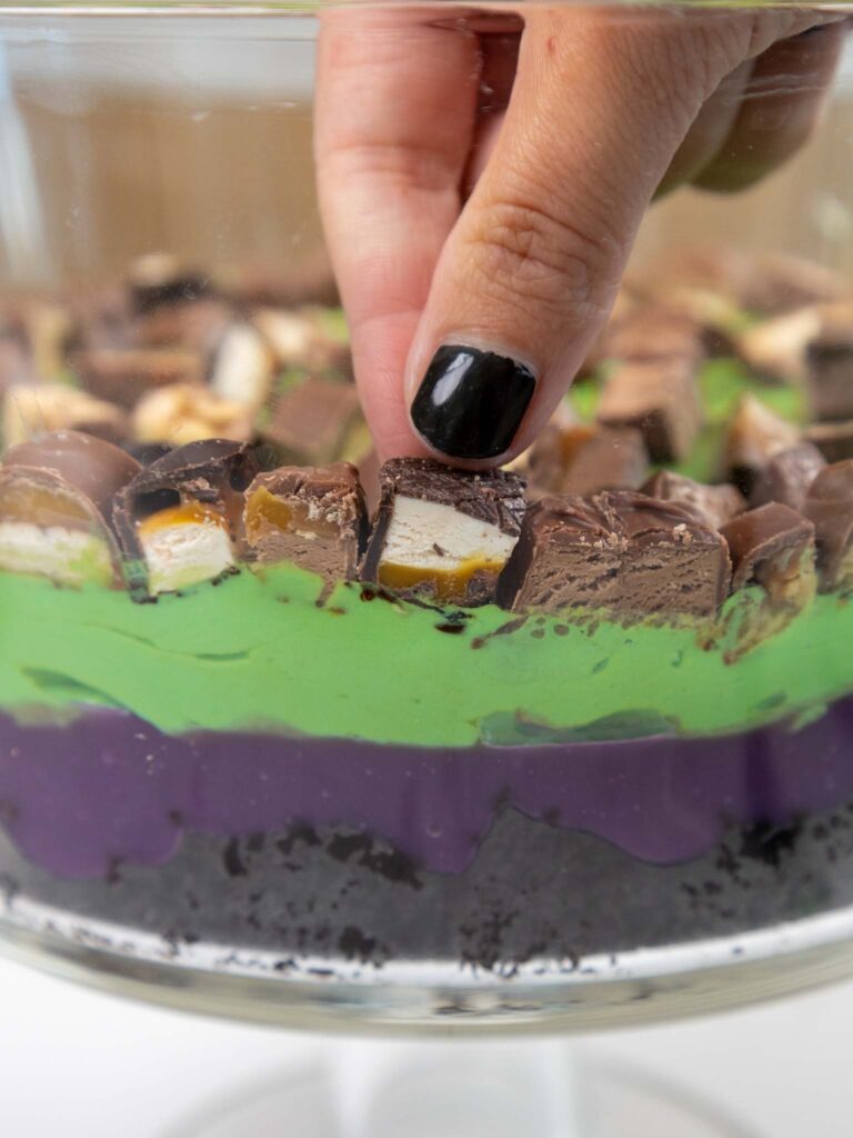 image of a halloween trifle being assembled with chocolate cake, pudding, and chopped up candy bars