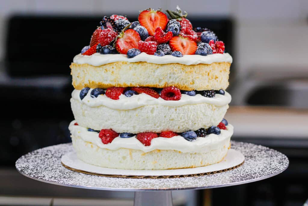 image of a layered angel food cake decorated with fresh berries and dusted with powdered sugar