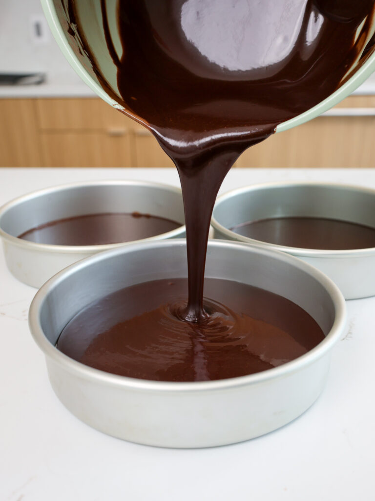 image of dark chocolate cake batter being poured into cake pans