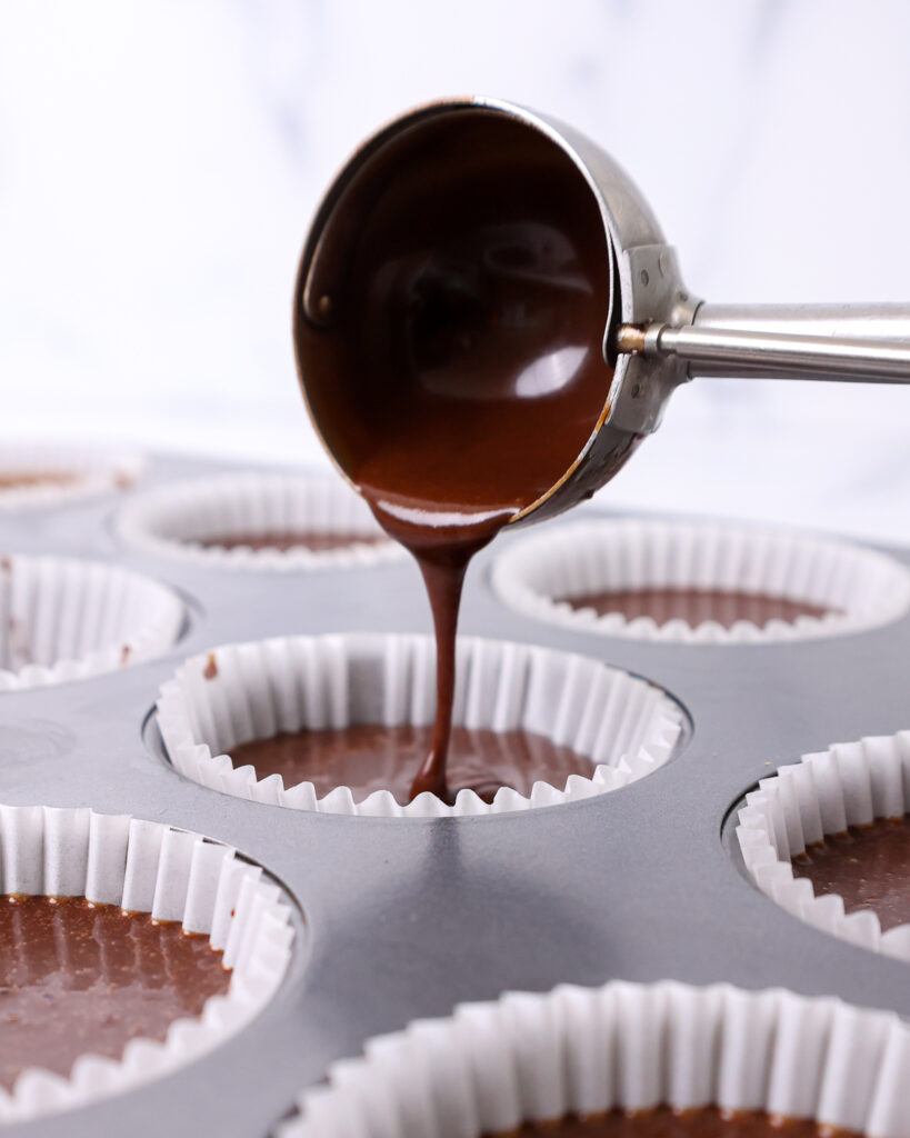 image of chocolate cupcake batter being poured into a cupcake liner with a cookie scoop