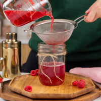 image of raspberry simple syrup being poured through a strainer