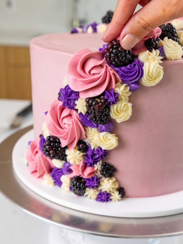 image of a fresh blackberry being pressed into buttercream swirls to decorate a blackberry mousse cake