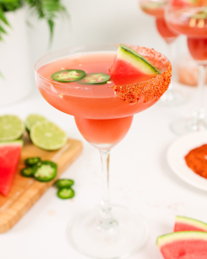 image of a jalapeno watermelon margarita in a margarita glass garnished with Tajín and jalapeño slices