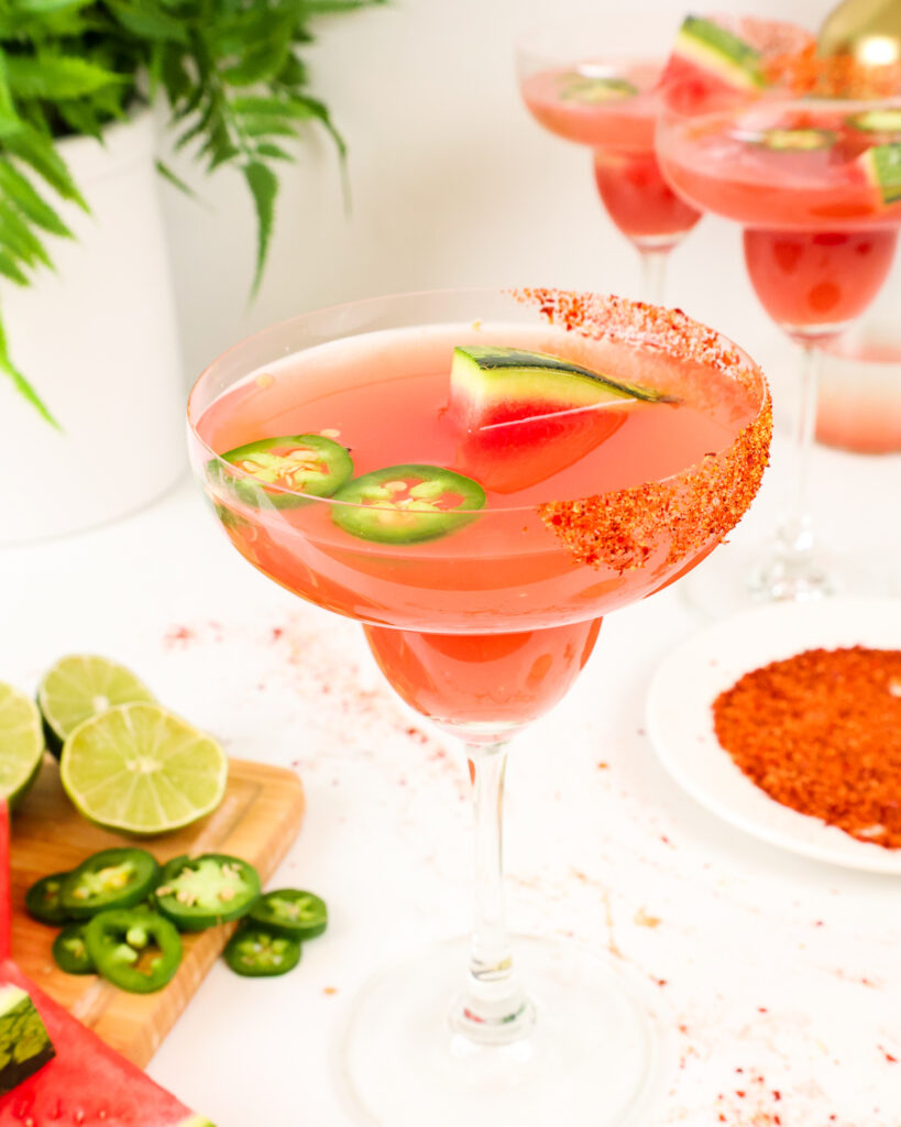 image of a jalapeno watermelon margarita in a margarita glass garnished with tajin and jalapeno slices