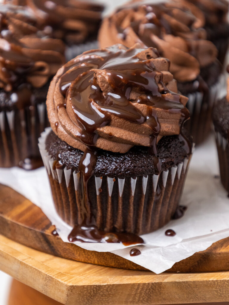 image of chocolate whipped cream frosting that's been piped on chocolate cupcakes and drizzled with chocolate syrup