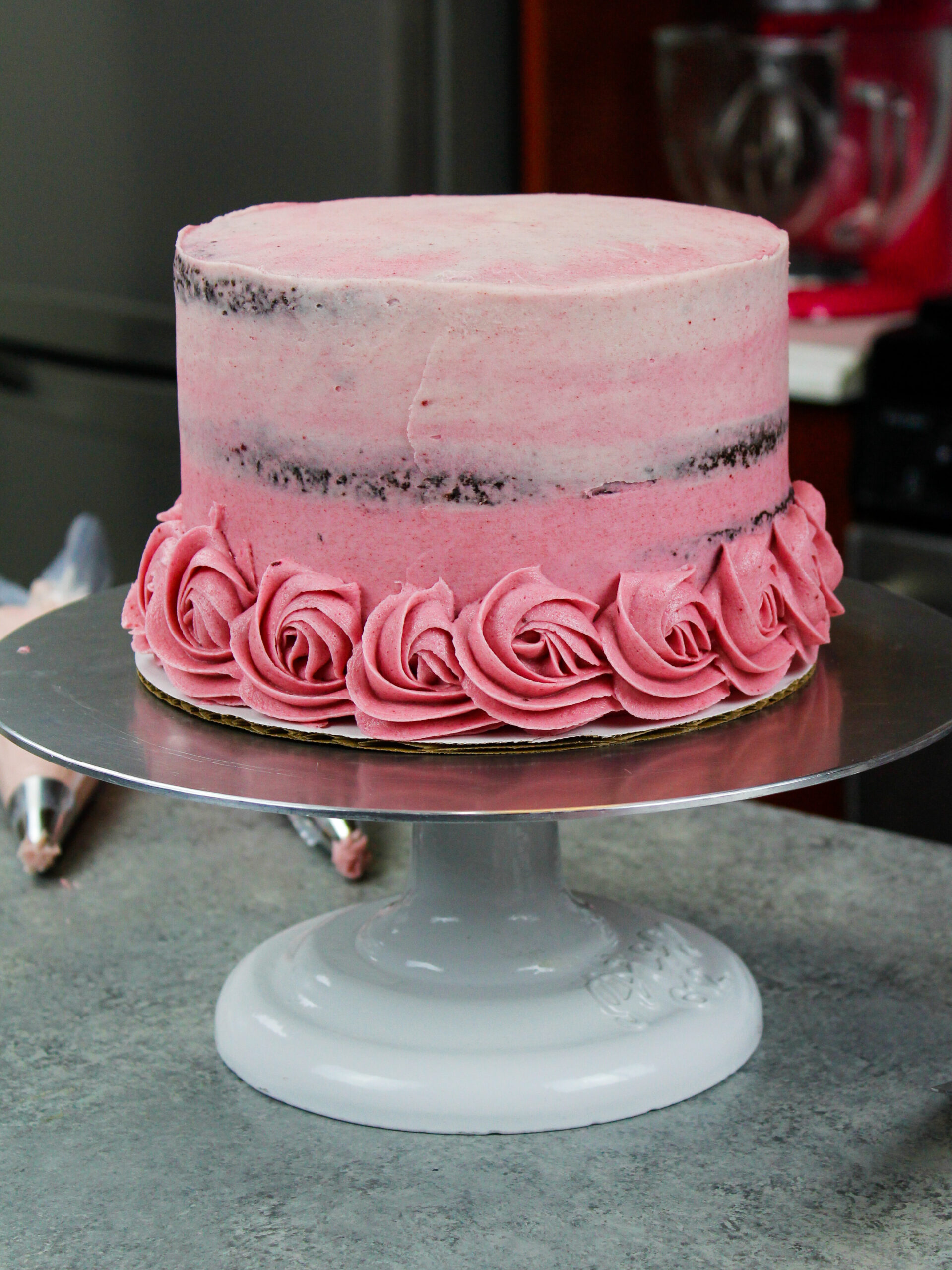 image of a chocolate cake that has been crumb coated with pink frosting to match the ombre buttercream rosettes that will be piped onto it to decorate it