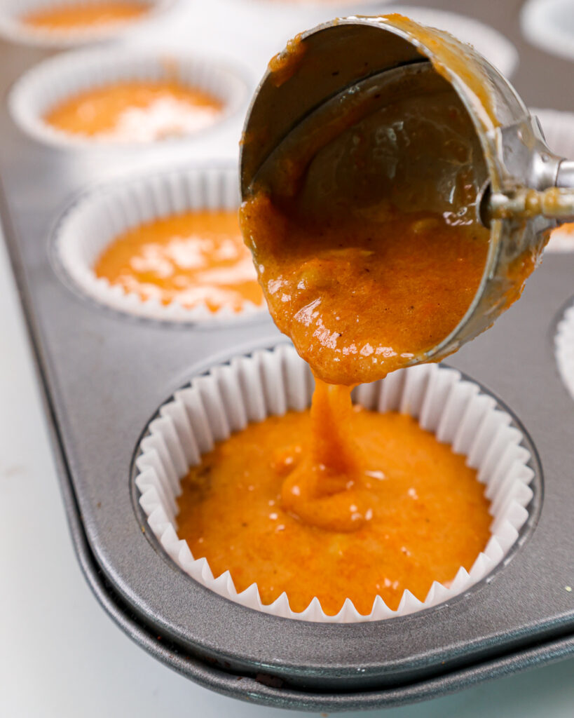 image of carrot cake cupcake batter being scooped into a muffin pan to make carrot cake cupcakes