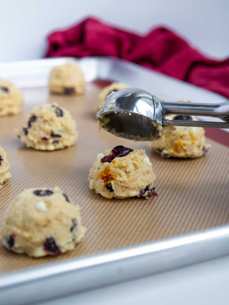 image of cranberry orange white chocolate cookie dough being scooped onto a silicone baking mat