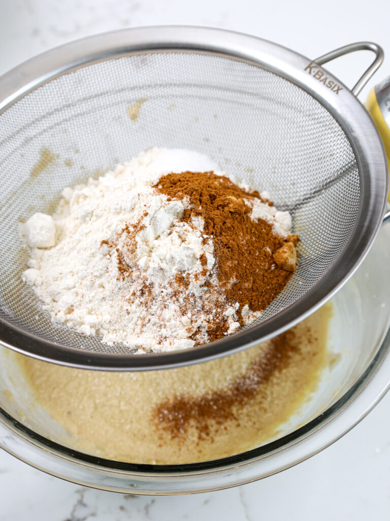 image of dry ingredients being sifted into wet ingredients to make spice cupcake batter