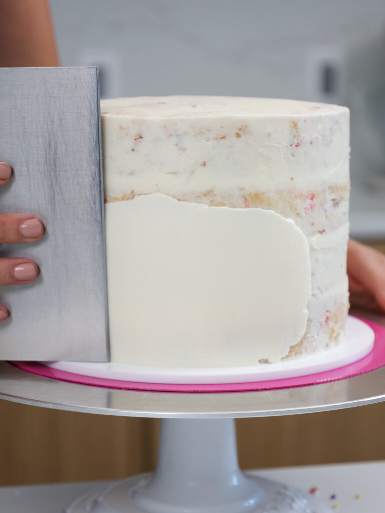 image of frosting being smoothed on front of a cake to make a llama face with buttercream