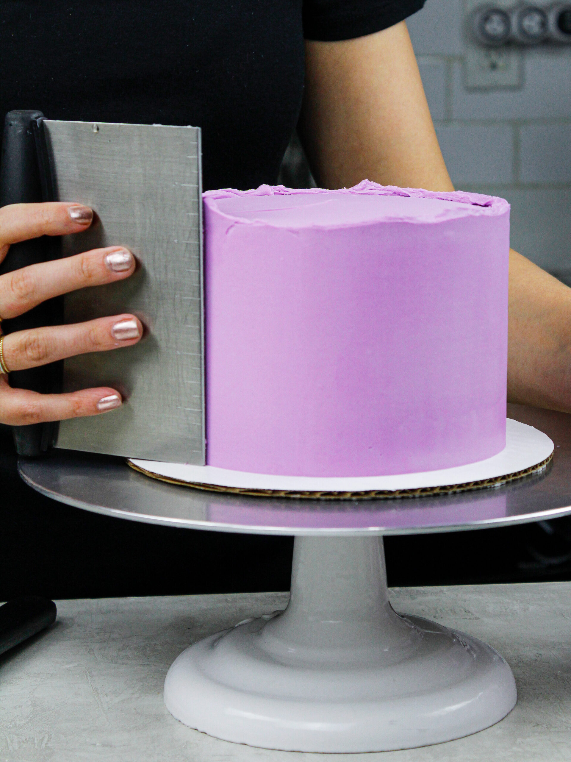 image of purple frosting being smoothed onto a cake with a bench scraper to show how to Frost a Cake Smoothly