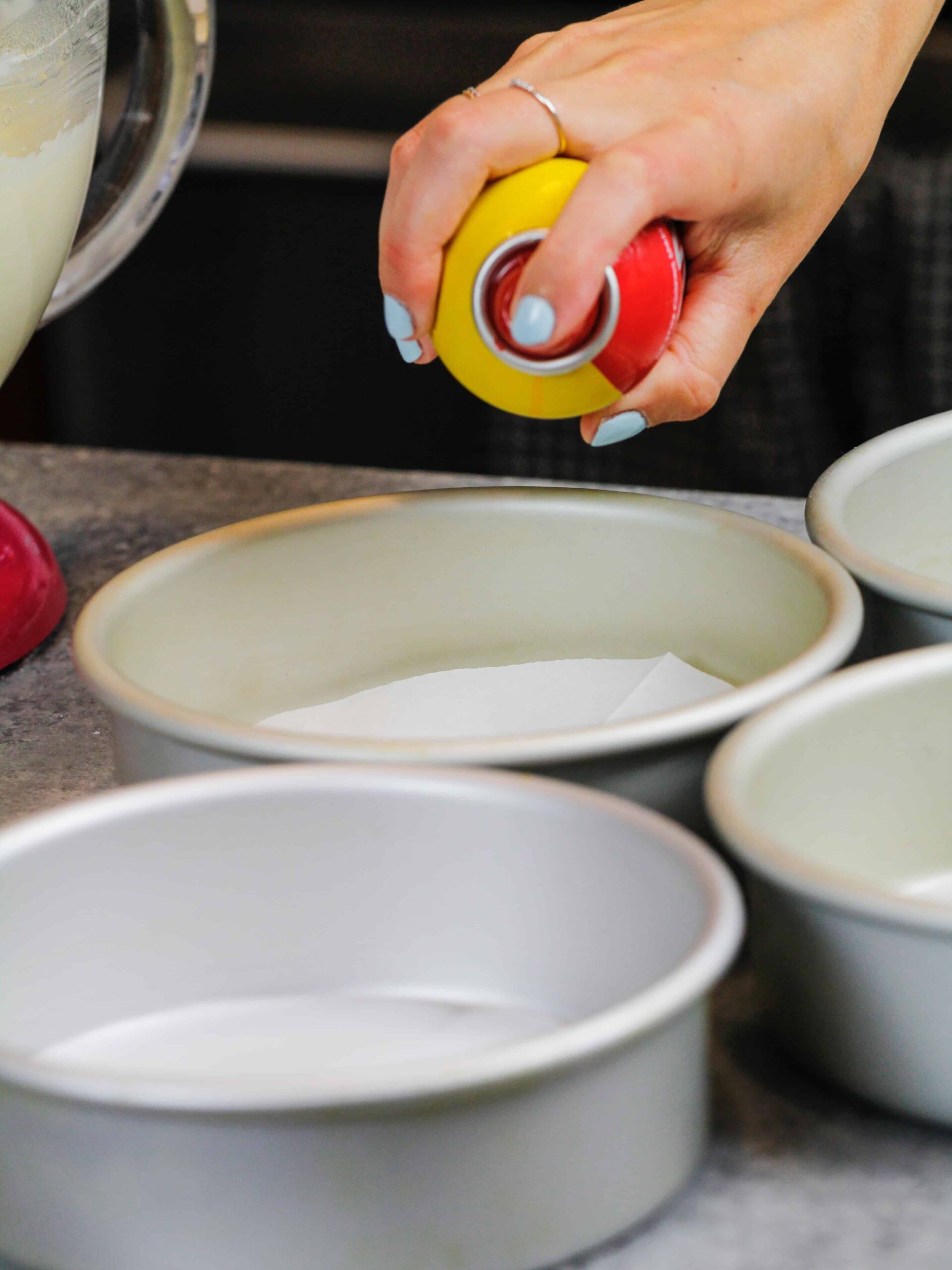 image of a cake pan being properly prepared with parchment rounds and non-stick spray to prevent the cakes from sticking to the pan.