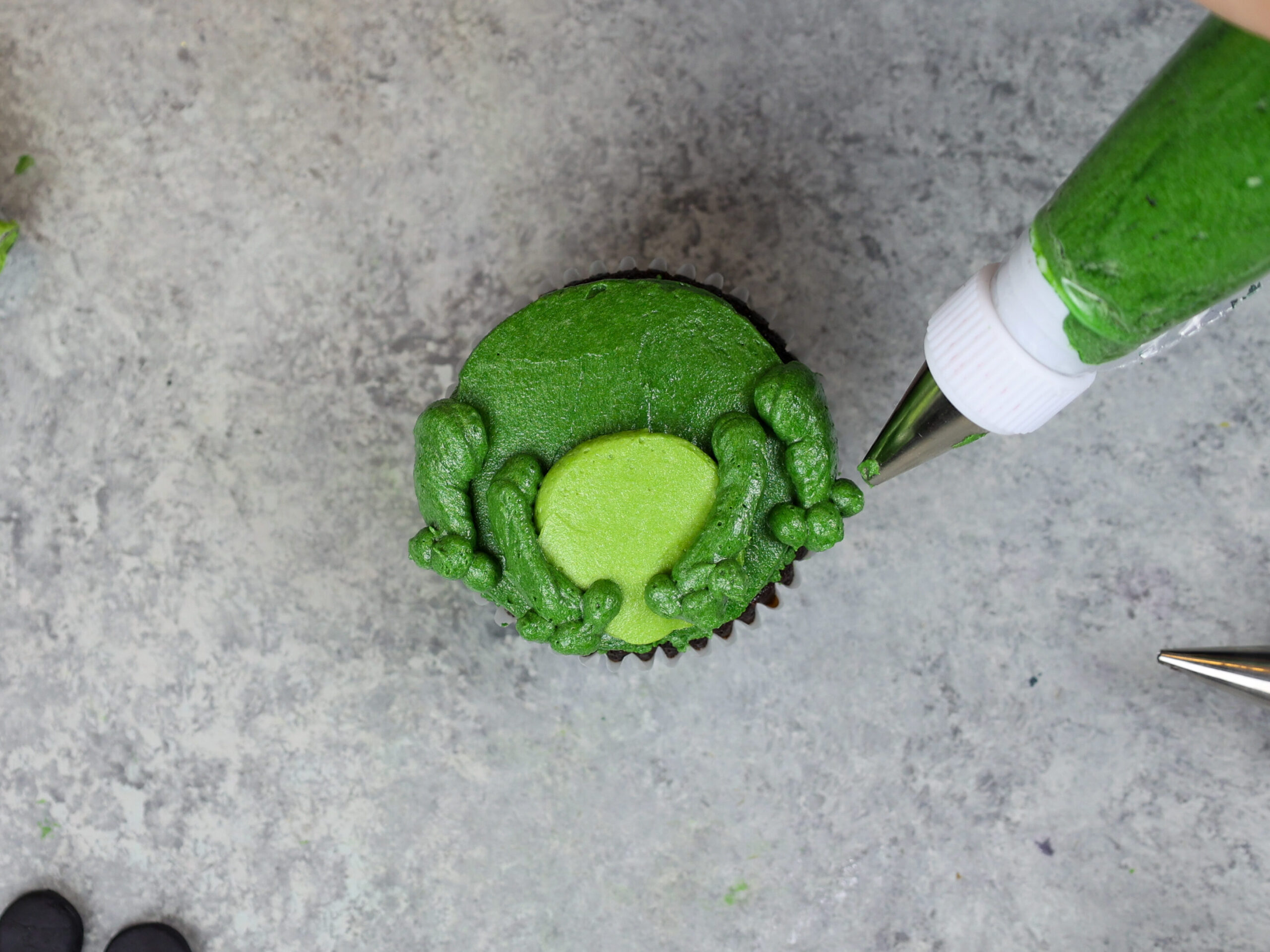 image of a frog cupcake being frosted and decorated with buttercream frosting