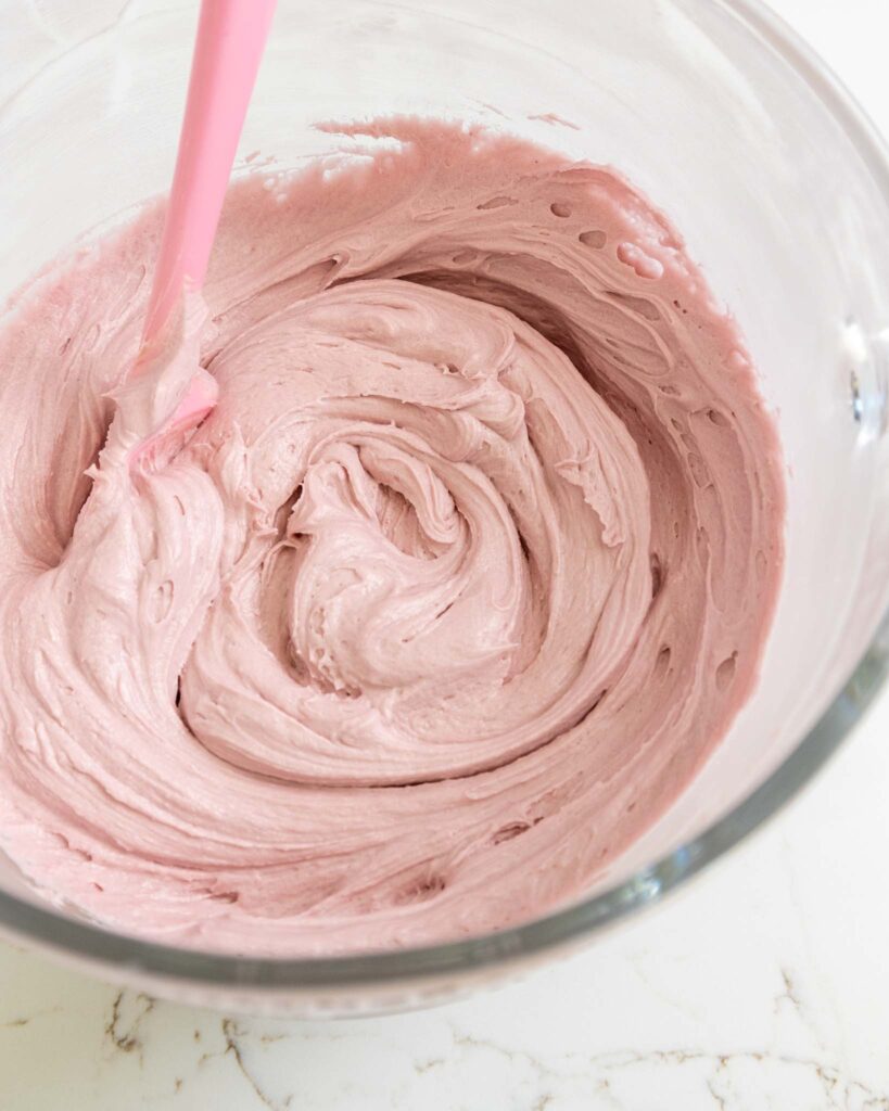 image of blackberry buttercream frosting being mixed together in a large glass bowl