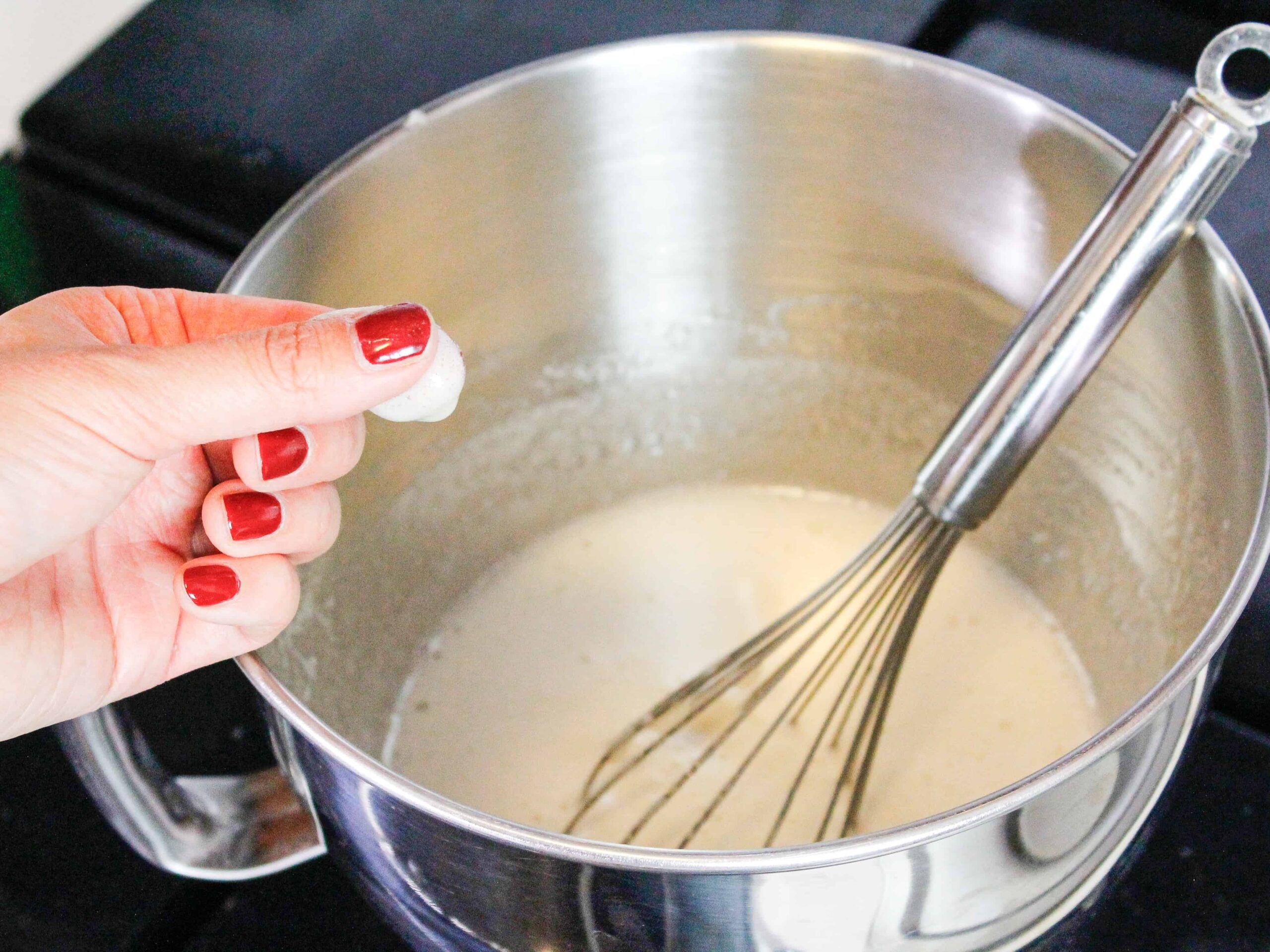 image of testing meringue base with fingers to make sure the sugar is fully dissolved before making it into swiss meringue buttercream