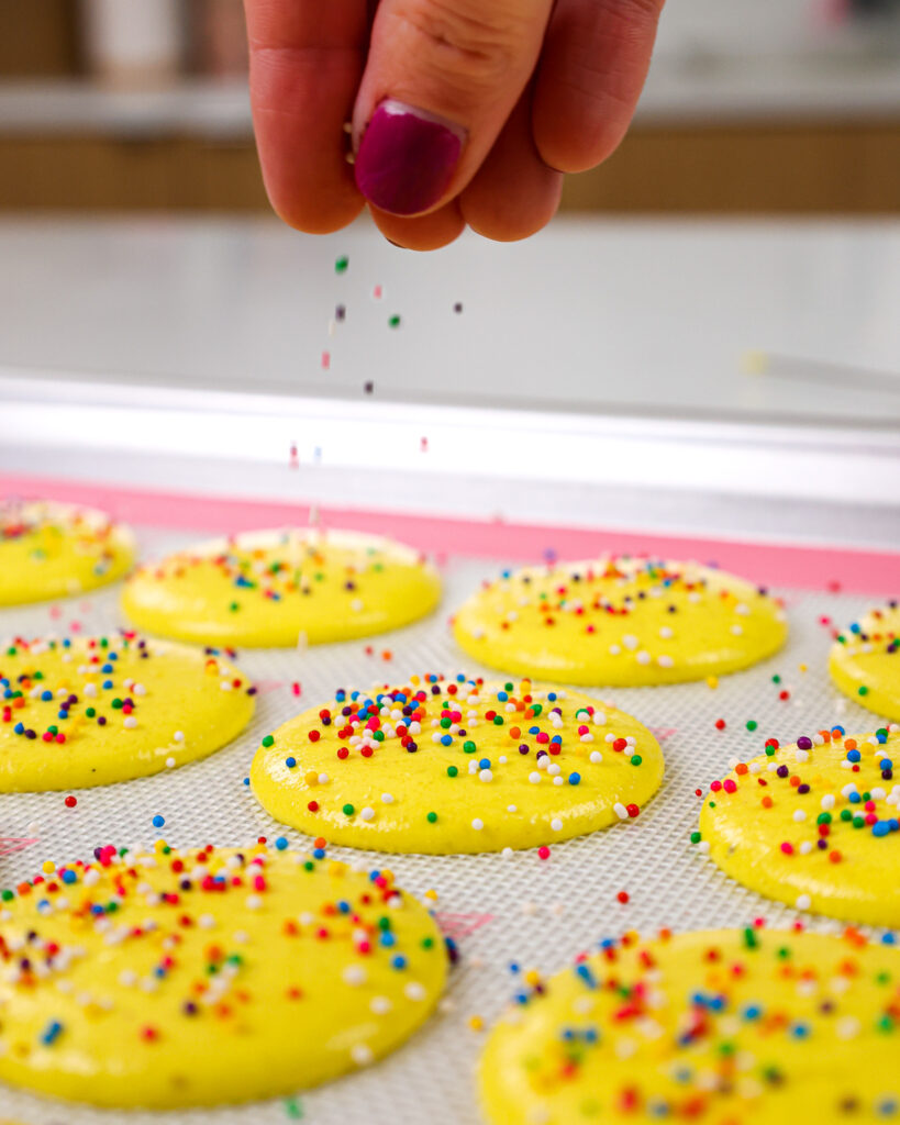 image of nonpareil sprinkles that are being sprinkled over macaron shells before they rest