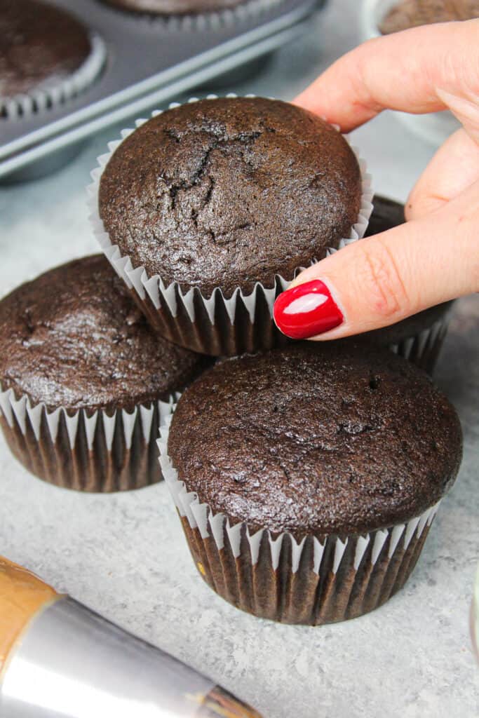 image of baked chocolate gluten free cupcakes stacked in a pile, ready to be frosted
