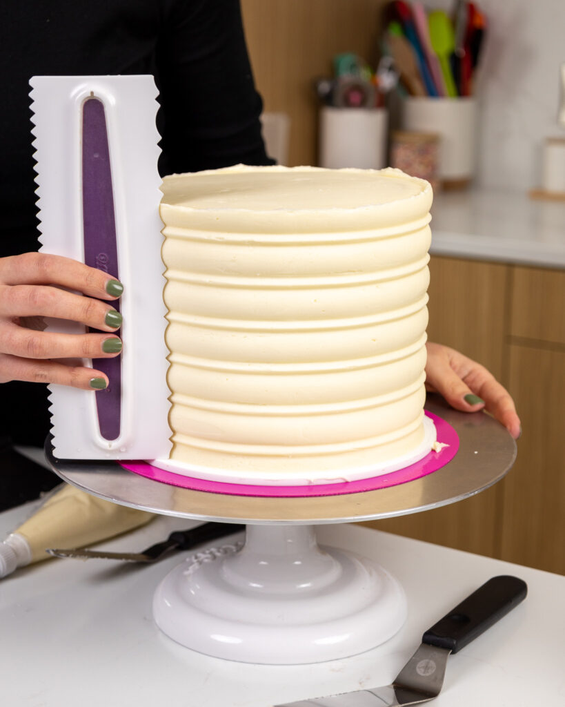 image of white chocolate buttercream being smoothed onto a cake using an icing comb
